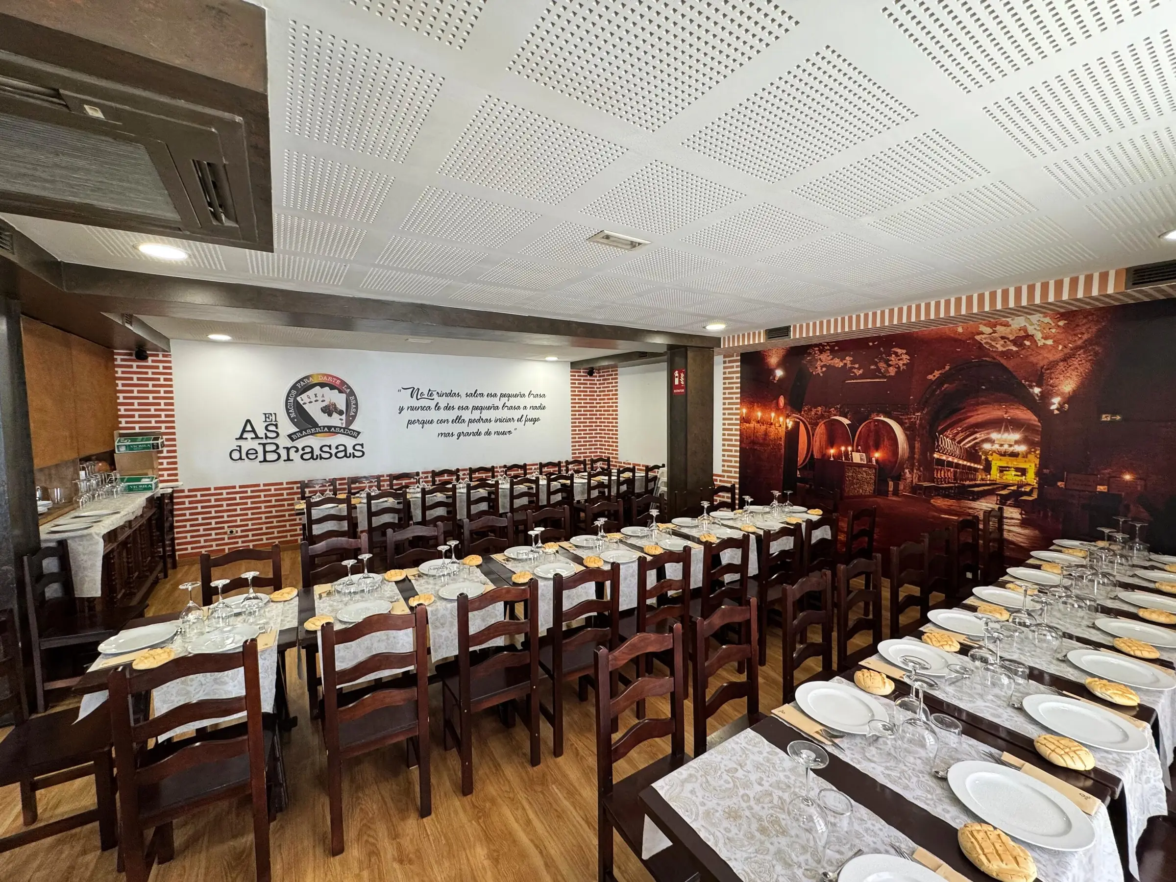 Comedor del As de Brasas con mesas montadas y el logotipo en la pared